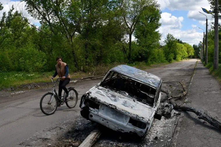 A man rides a bicycle past a car destroyed by shelling in a street in the village of Niu-York, Donetsk region, Ukraine.