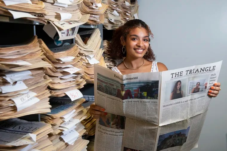 Kiara Santos, a senior at Drexel University, became the first Afro-Latina editor-in-chief of The Triangle, which is now a digital newspaper. She stands beside their paper archives. She holds the newspaper that contained her first published story.