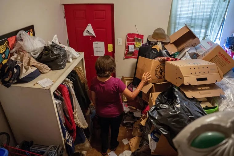 An East Kensington woman with hoarding disorder makes her way through the small aisle in a living room packed with boxes, clothes, other belongings and trash. Sue is a member of Clutterers Anonymous and is trying to slowly clean her house.