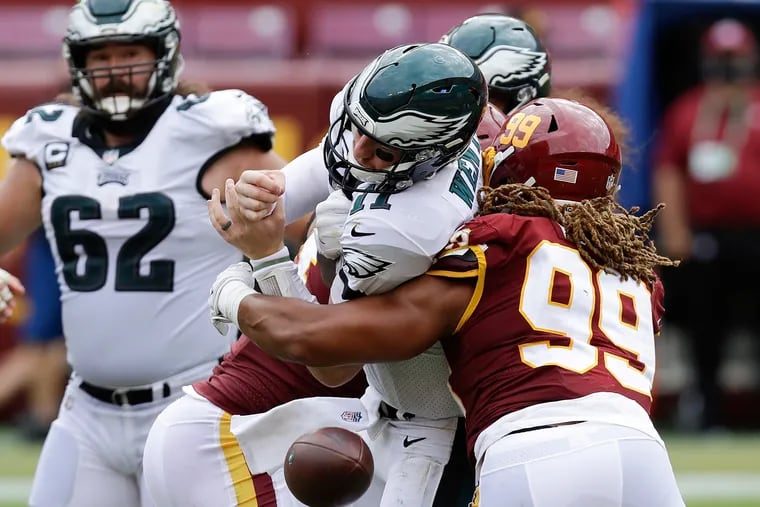 Eagles quarterback Carson Wentz fumbles the ball after being hit by Washington nose tackle Daron Payne (left) and defensive end Chase Young in the fourth quarter on Sunday.