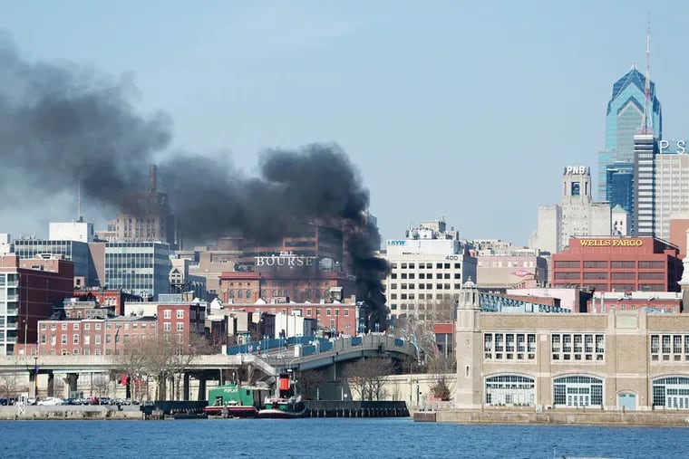 Smoke can be seen from Camden as Philadelphia firefighters work on a persistant fire at Suit Corner and adjacent buildings at 3rd and Market Streets Wednesday, April 9, 2014. ( DAVID SWANSON / Staff Photographer )