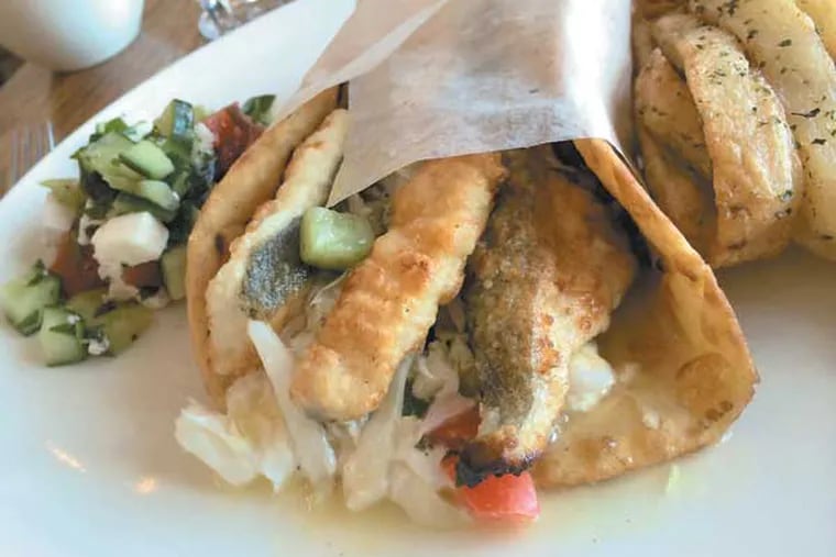 The "fish gyro" sandwich, a signature lunch item at the new Estia Taverna in Marlton (formerly Pietro's); it's made from pan-crisped halibut, finished with Greek yogurt, feta, slaw and relish of cucumbers, tomatoes and olives.  (Craig LaBan / Staff)