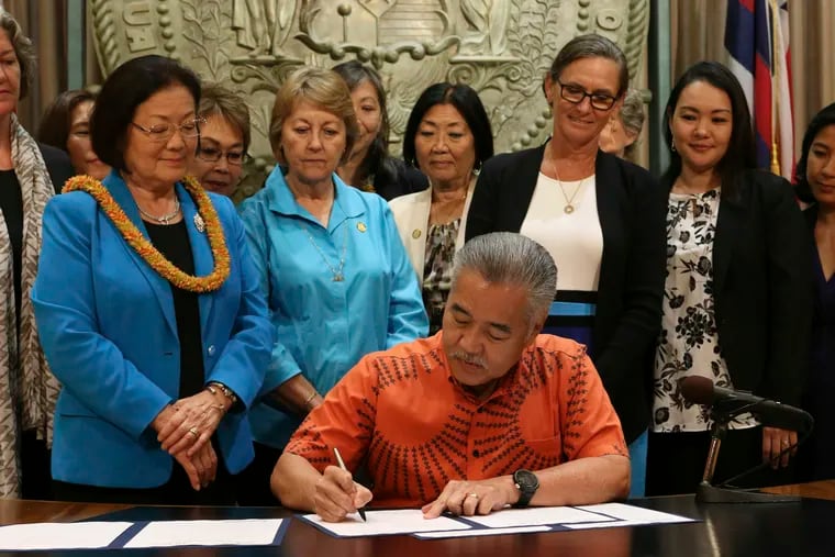 Hawaii Gov. David Ige, surrounded by members of the bipartisan Hawaii Women's Legislative Caucus and U.S. Sen. Mazie Hirono (wearing a lei), signs legislation in Honolulu, Tuesday, July 2, 2019, making Hawaii the first state in the U.S. to remove a requirement that a person be a victim of sex trafficking to have a prostitution conviction erased.