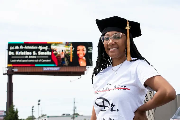Kristine Smalls, a recent graduate from the Philadelphia College of Osteopathic Medicine with a doctor of psychology degree, near the billboard her mom surprised her with in Camden on Sunday.