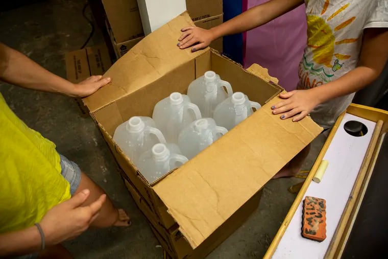 Jodi Cutaiar, 41, of Sellersville, Pa., and her eight-year-old open a box of the bottled water they use for cooking and drinking in their basement earlier this month. Their home's well is contaminated with PFAS.