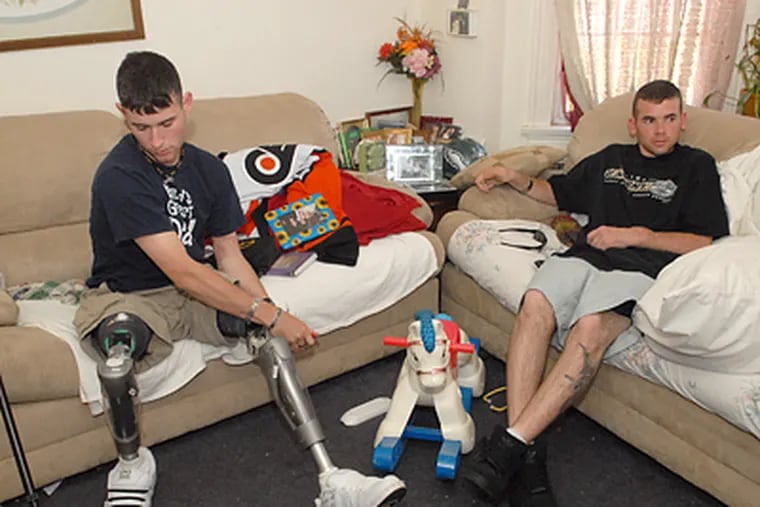 Ray Hennagir puts on his legs at his fiancee's house in Woodbury as his friend Kevin Hardin sits at right. Hennagir lost both legs and part of one hand when he stepped on an IED in Iraq. (Peter Tobia/Inquirer)