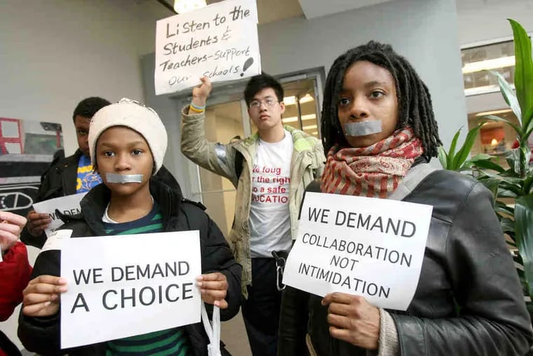 Protesting outside the School Reform Commission meeting are students Stefan Small (left), Wei Chen, and Darlene DeVore. The tape represents what they say are their silenced voices.