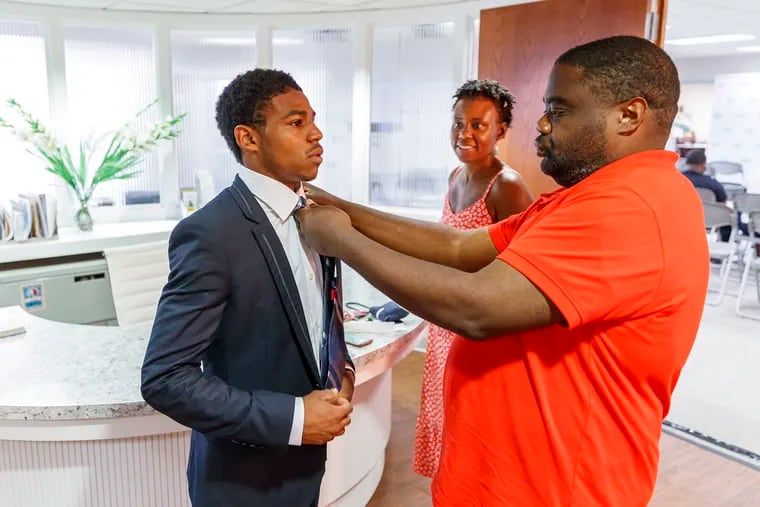 Devante Johnson, left, who graduated on Thursday June 27, 2019, in the Philadelphia OIC Smart Energy Technical Training Program, needed a little help from a passer-by, Robert Miller, right, to get his necktie straight for the ceremony. NaDerah Griffin, center, Devante's aunt, center, looks on approvingly.