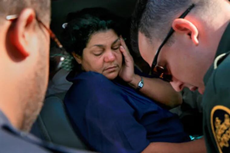 Cuban refugee Emilia Vasquez Sevilla waits as officers take roll call while detainees sit inside a van outside the Longboat Key police station.