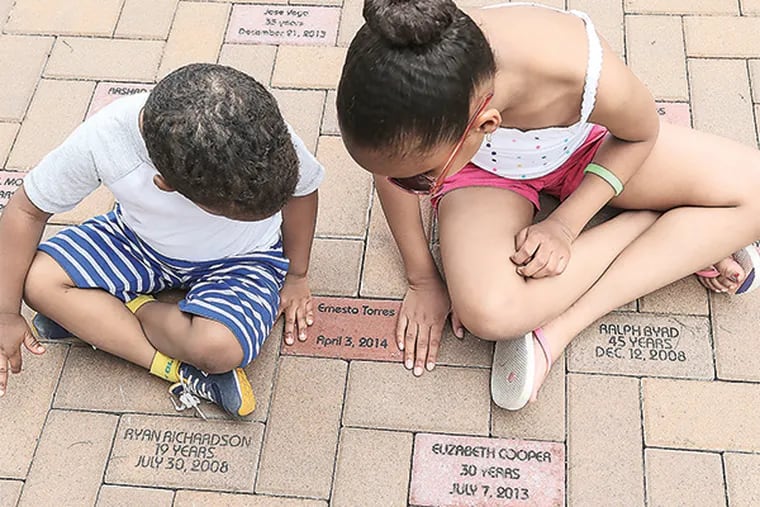 TJ, 2, and his sister Isys,10, Mosby look at the brick of their uncle Ernesto Torres Jr., 22, killed April 3, 2014. The owner of a Camden demolition company has been laying bricks for the city's homicide victims since 2007. There are more than 500 bricks out there now.