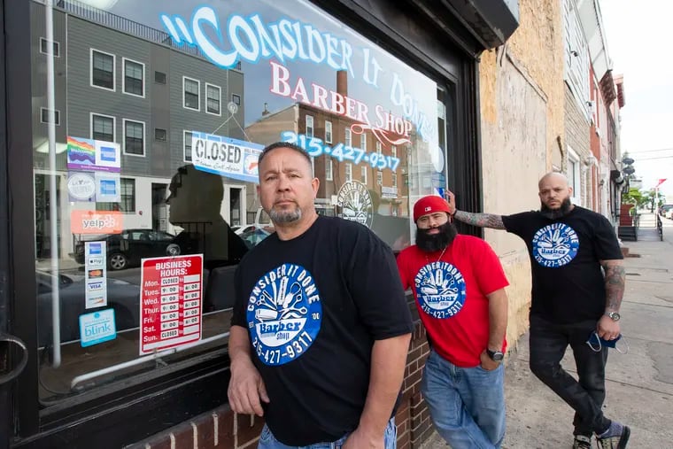 From left to right: Alcides Franceschini, owner of Consider It Done Barber Shop, Eric Robledo, and Nathaniel Zenon, stand outside the closed shop on May 5, 2020. As barbers sit at home due to the mandated coronavirus closures, many worry not just about their jobs but the future of barbershops in neighborhoods where they are more than just a place to get a hair cut.