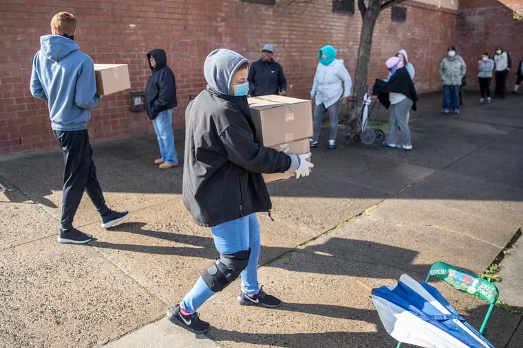 Odette Smith carries away boxes of food from the Cohocksink Recreation Center in Kensington while other residents wait in line. In addition to sites offering boxes of food, the city announced that it will open sites offering grab-and-go meals for seniors and diapers and supplies for babies and toddlers.