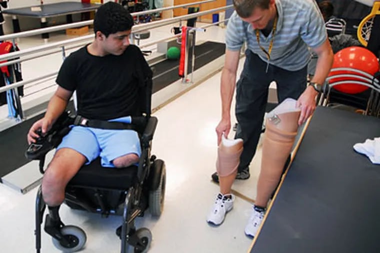 Physical therapist Ryan Brown (right) stands upright the prosthetic legs of Asaad Mahmoud, 15 of Palestine, at Shriner's Hospital. He's in Philadelphia receiving treatment for injuries from a bomb in the Gaza Strip. He lost both legs and his left arm. (Sarah J. Glover / Inquirer)
