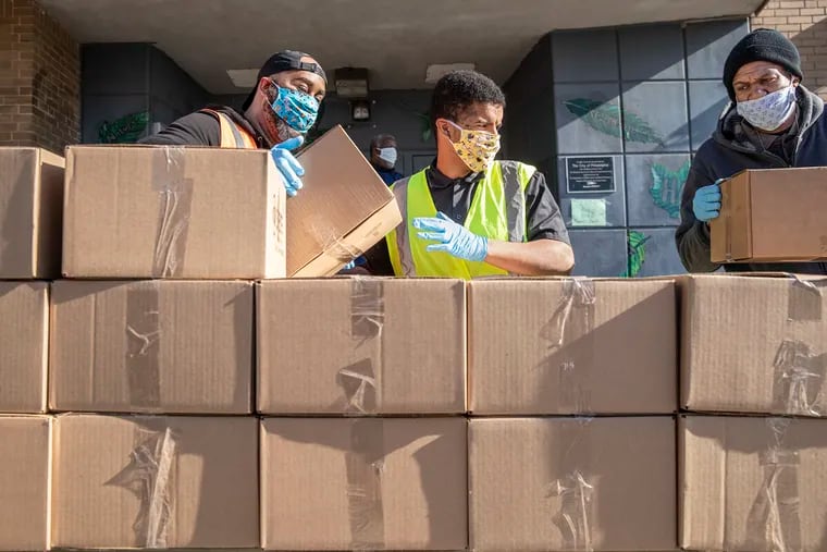 Idris Hodge, left, Juan Reina, center, and James Scott, right, stack boxes of food on a distribution table at the corner of 25th and Diamond on Monday April 6, 2020.