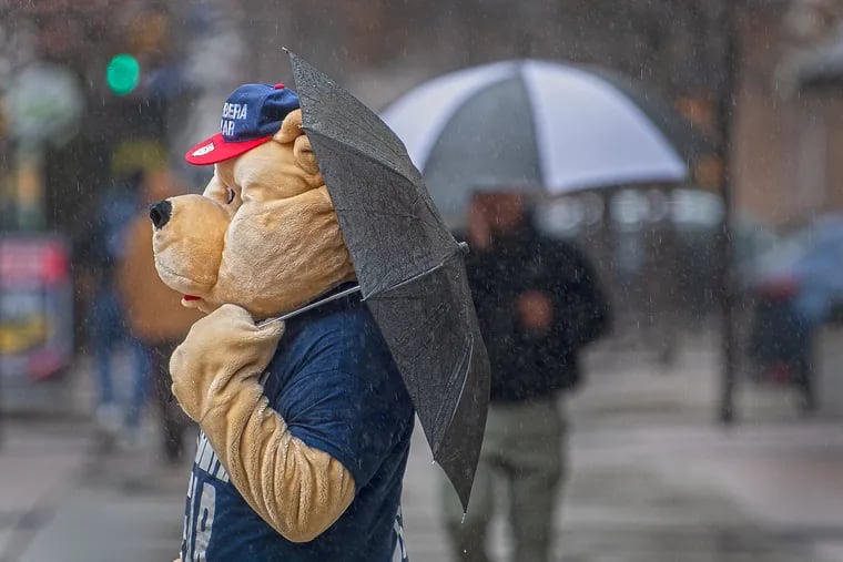 A person wearing a bear costume (Gary Barbera's auto mascot) shields from the rain with an umbrella outside the 2022 Philadelphia Auto Show.