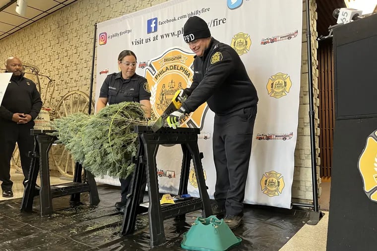 Philadelphia Fire Commissioner Adam Thiel demonstrates how to safely cut a Christmas tree during an annual event to promote holiday season safety at the Fire Administration Building on Monday.