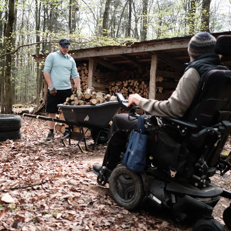 Army veteran Adam Perry loads and stacks firewood while Todd Gladfelter looks on from his motorized wheelchair, in New Ringgold, Pa., on April 28, 2024.