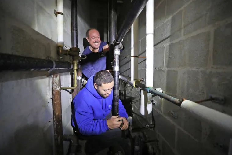Plumbing apprentice Antonio Lopez, 20, learns the ropes from mentor Chris Hamler, 47, reconnecting tail pieces for toilets at Benjamin Franklin Elementary School.