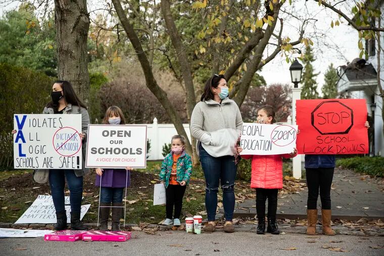 (left to right) Jessica Bradbury and Emma Bradbury, 7, of Lower Providence Township, Elyse Singer, 3, Jennifer Singer, Abby Singer, 8, and Kayla Singer, 11, of Montgomery Township, gathered outside the Wyndmoor home of Montgomery County Commissioners Chair Val Arkoosh Sunday to protest the county's decision to close all K-12 schools for two weeks beginning Nov. 23. The song "Safety Dance" by Men Without Hats played on repeat from a portable speaker, as parents and students held protest signs in the street.