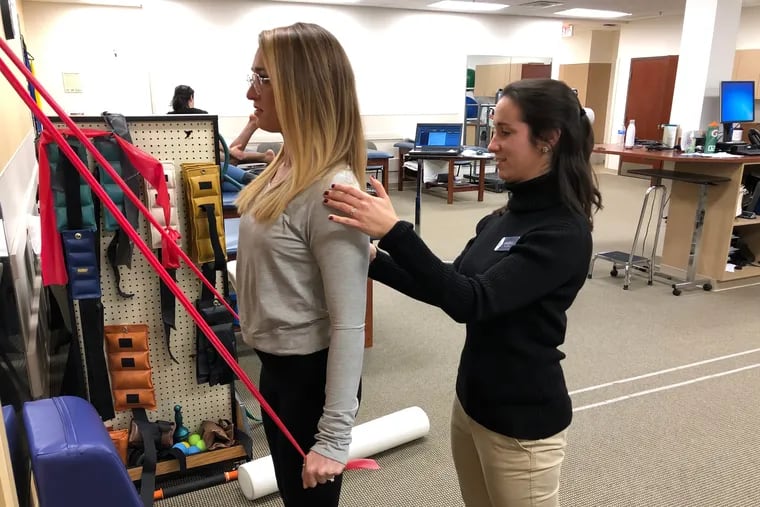 Rothman physical therapist Angela Lenzo shows patient Betsy Mamtsis how to perform a theraband extension to strengthen scapula musculature.