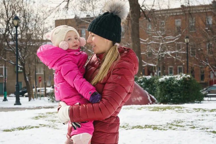 Catherine Milano, with her daughter Ella, in Dickinson Square Park after snow fell in the Philadelphia region on Friday. Staying indoors might be a better option Tuesday morning as wind chills tumble into single digits.