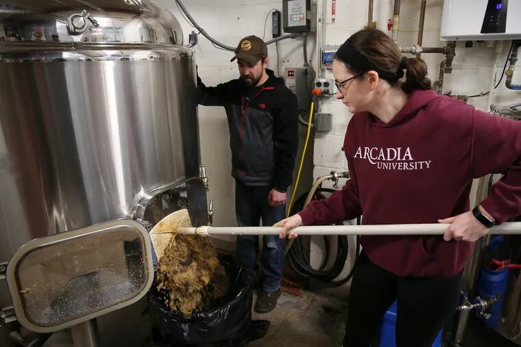 Co-founder Jeff Mulherin, left, watches Arcadia University senior Nicole Hassett clean out grain from the mash tank at Crooked Eye Brewery in Hatboro, Pa., on Saturday, April 6, 2019. Students in Arcadia University's "Untapped" seminar about beer visited the brewery to learn about how beer is made.