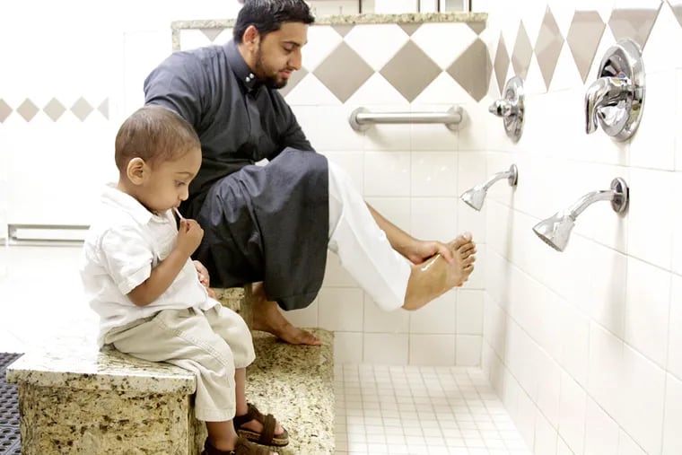 Maheen Khan washes his feet before the meal and prayer as his son, Ibrahim, sits with him. Khan is the organizer of the &quot;iftar&quot; at the Islamic Society of Greater Valley Forge. ELIZABETH ROBERTSON / Staff Photographer