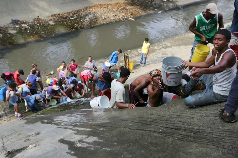 People collect water from an open pipe above the Guaire River during rolling blackouts, which affects the water pumps in people's homes, offices and stores, in Caracas, Venezuela, Monday, March 11, 2019. The blackout has intensified the toxic political climate, with opposition leader Juan Guaido blaming alleged government corruption and mismanagement and President Nicolas Maduro accusing his U.S.-backed adversary of sabotaging the national grid. (AP Photo/Fernando Llano)