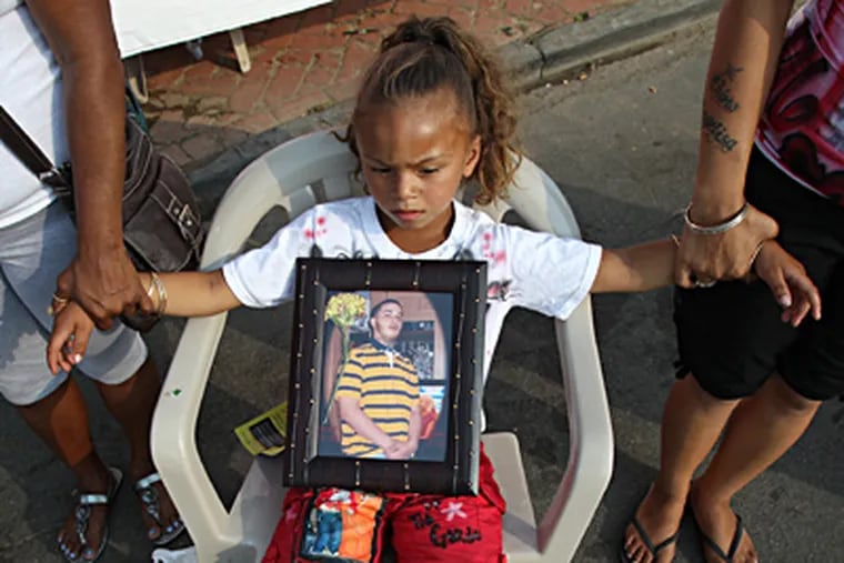 Angelina Nu&#0241;ez joins hands with relatives while on her lap is a photograph of her brother Reynaldo Moralez, one of 13 people slain in Camden in July. RON CORTES / Staff Photographer