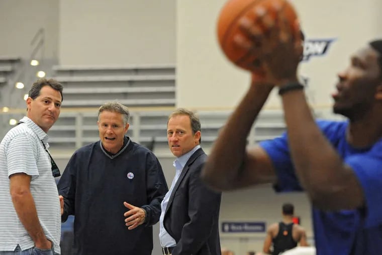 PHOTOS: CLEM MURRAY / STAFF PHOTOGRAPHER Sixers coach Brett Brown , managing owner Josh Harris (right) and co-managing owner David Blitzer (left) watch injured first-round draft pick Joel Embiid shoot baskets from a chair.