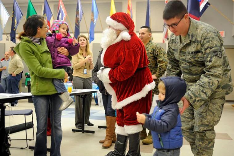 Santa talks with Sarra Shelly (left) and her daughter Julia, 2, as they arrive to pick up holiday meal kits at Joint Base McGuire-Dix-Lakehurst on Dec. 10, 2014.  Her husband, Dustin Shelly, is deployed in Germany with the Air Force. At right is Benjamin Floyd, also in the Air Force, with his son Daniel, 2.