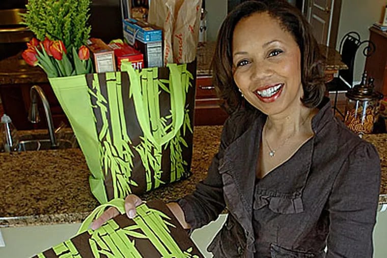 Tyra F. Hodges, one of the co-owners of Tymel Style, LLC, holds one of her "green" bags with another one on the counter stuffed full of products. ( Clem Murray / Staff Photographer )
