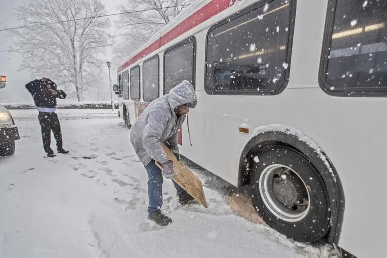 Jeffrey Fisher, right, who works for the City Street Department throws some rock salt in front of the left back wheel of a SEPTA bus that got stuck on Germantown Avenue due to the icy conditions and was blocking traffic during the storm on March 7, 2018.