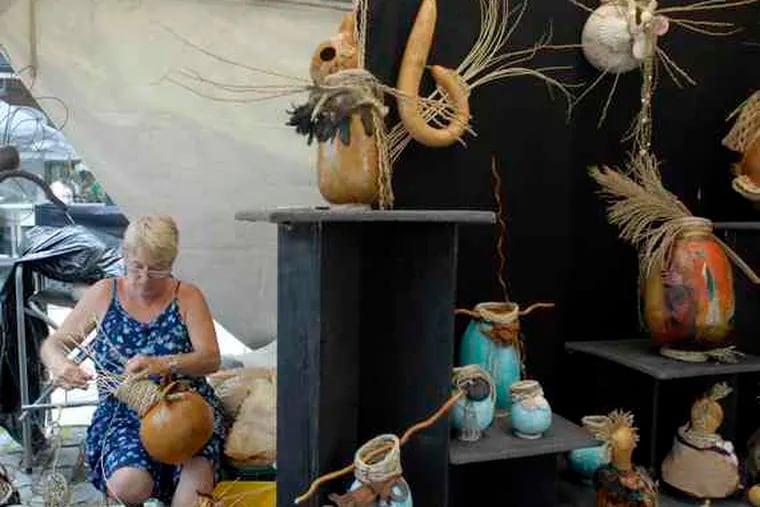 Bonnie Eastwood of Hudson, Fla., who crafts art from straw and gourds, works on one of her pieces in her booth at the 21st annual Manayunk Arts Festival. The festival, featuring the work of 275 artists, ends Sunday evening.
