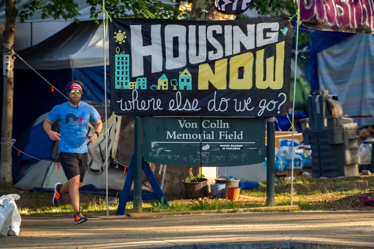 A runner passed the entrance to homeless encampment at Von Colln Memorial Field on the Parkway during this summer's protest. Organizers of the protest negotiated a deal to provide residents with shelter, but housing insecurity remains a big problem in Philadlephia.