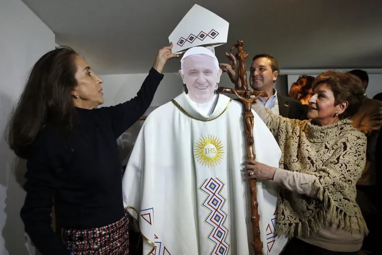 In this Aug. 29, 2017 photo, fashion critic Pilar Castano, left, and designer Regina Bastidas dress a cardboard cutout of Pope Francis with the vestments he would wear during a visit to Colombia, in Bogota, Colombia.