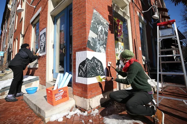 Artist Jeremiah Jordan (left) and Golden Collier (right) install two wheatpaste pieces outside Giovanni’s Room bookstore, part of the Asian Arts Initiative's multi-site "Unity at the Initiative" exhibition celebrating the city's trans and gay artists of color.