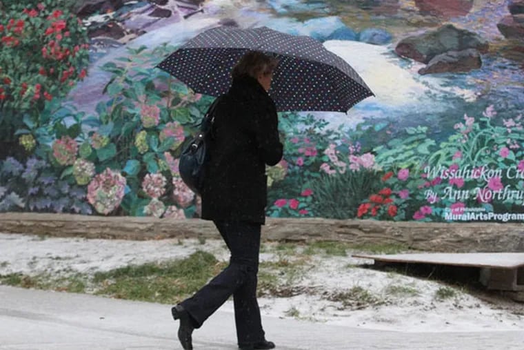 A pedestrian makes her way on a snow-covered sidewalk along Germantown Ave. in Chestnut Hill with the mural "Wissahickon Crossing" by the Mural Arts Program behind her.   ( Charles Fox / Staff Photographer )