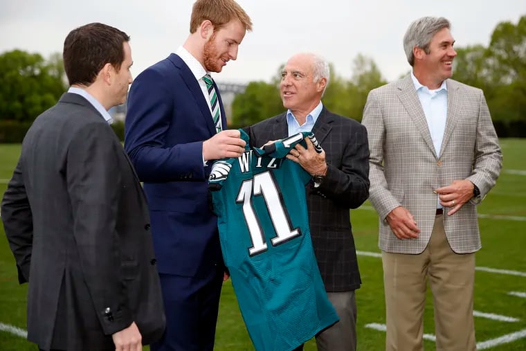 Eagles first round draft pick Carson Wentz, holds his jersey with Eagles owner and chairman Jeffrey Lurie in April 2016. Howie Roseman is on the left, and coach Doug Pederson on the right.