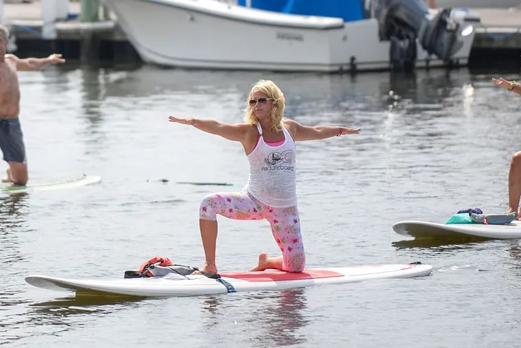 Cheryl McBride with OC Paddleboard leads a yoga class at Seaview Harbor in Longport. (BEN MIKESELL/Staff Photographer)