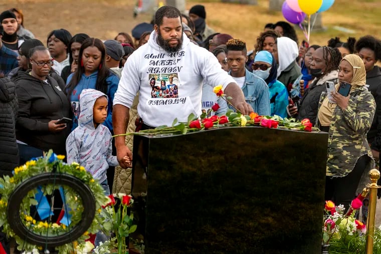 Maurice Taylor holds the hand of his nephew Rahsean Wayne on Thursday as he places a rose on the just-unveiled headstone that marks the graves of the 12 victims of last year’s Fairmount rowhouse fire. Wayne lost his mother and siblings in the fire.