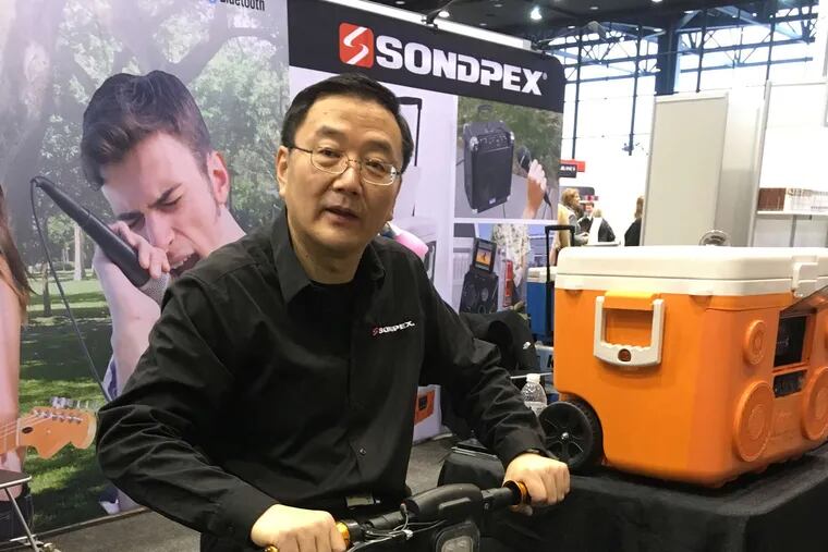 Sondpex vice president Chuck Chen rides a Fold & Zip electric scooter. Near him is the KoolMax cooler.