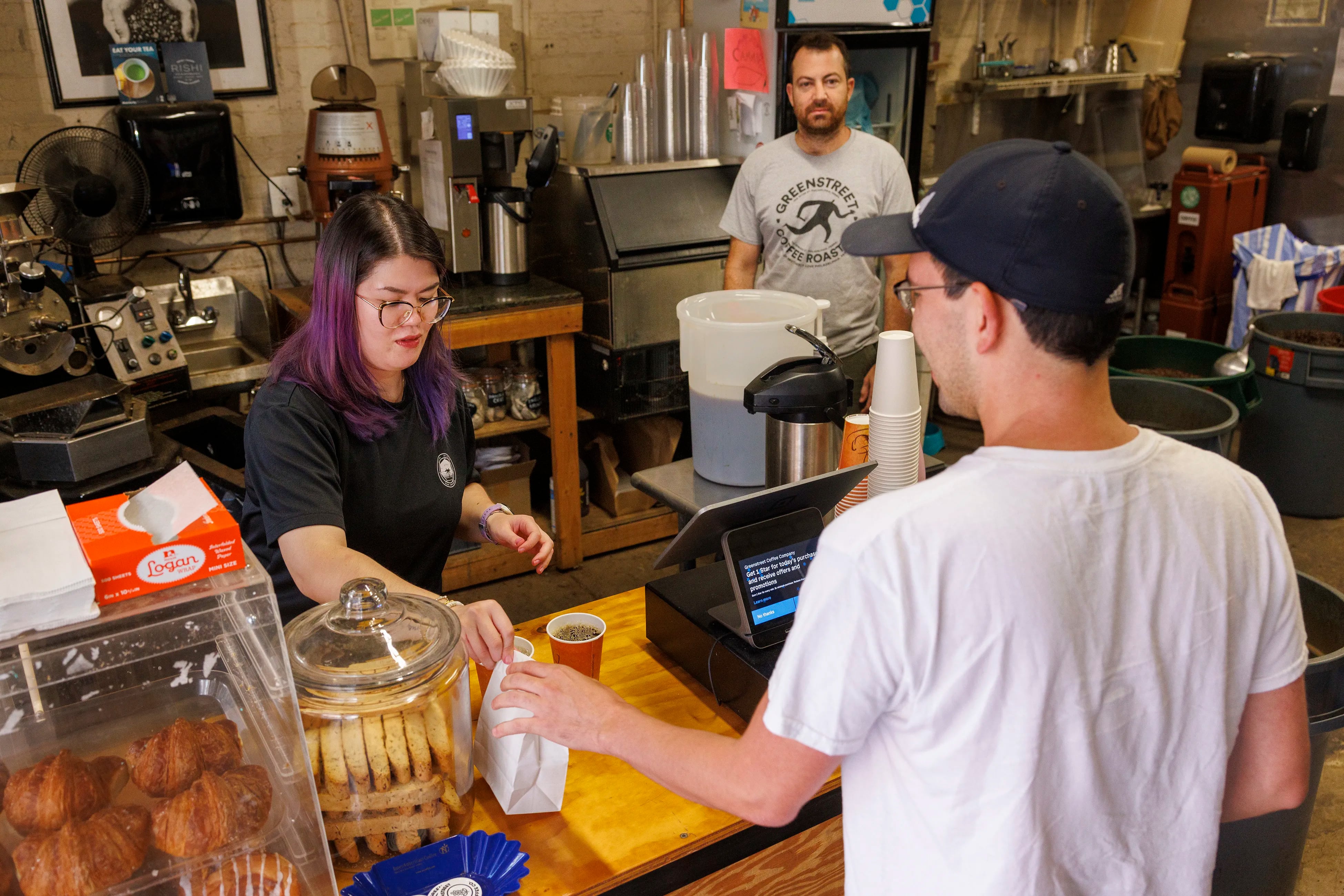 Barista Lucy Lu (left) attends to customer Christian Gray with owner Chris Molieri in background at Greenstreet Coffee Roastery. 