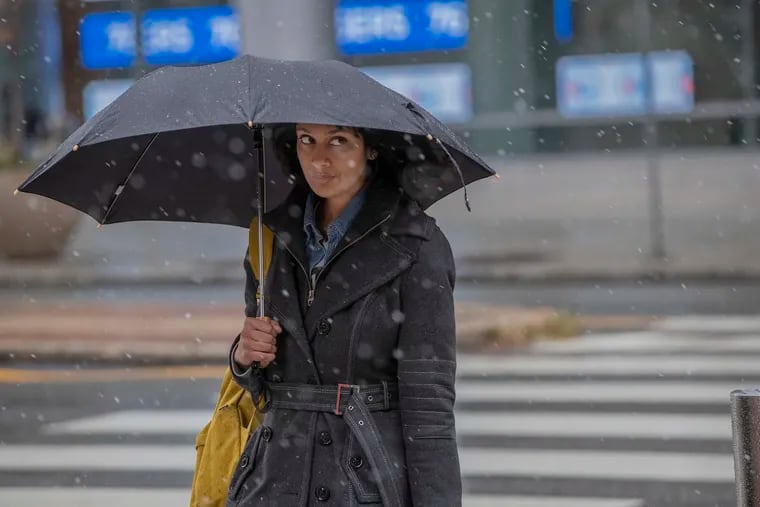 A pedestrian crossing Broad Street with umbrella in hand looks to the snow flakes falling in Center City shortly before noon on Tuesday Nov. 12, 2019.