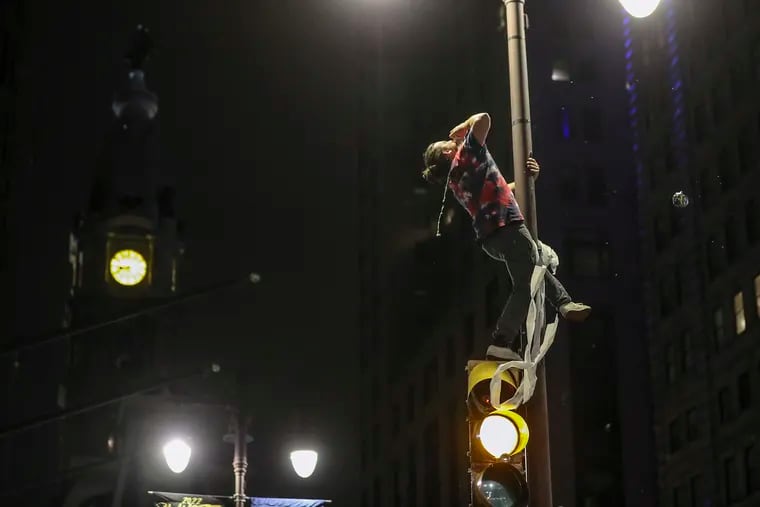 Sean Hagan, 29, of South Philly, shotguns a beer thrown to him from revelers below while atop a pole at Broad and Sansom Streets Sunday night after the Phillies NLCS win.