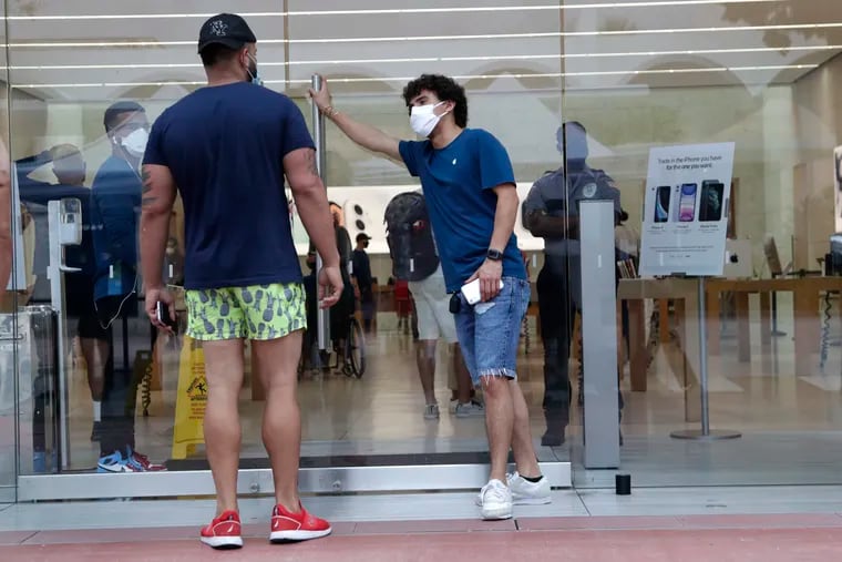 An employee wearing a protective face covering (right) monitors the flow of customers at an Apple retail store in Miami Beach on June 17.