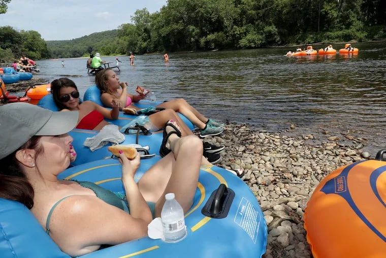 Kelly Radzai, 51, left, eats lunch with her daughter, Ally Radzai, 17, center, and Savannah Wood, 16, while taking a break from tubing on the Delaware River on August 5, 2019.  They were resting on what Greg Crance, owner of Delaware River Tubing, calls "Adventure Island." It sits on the Delaware River near Kingwood, NJ. He owns the island where he serves food from a floating grill.