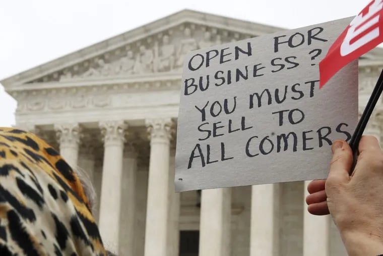 A woman holds up a sign as people gather outside of the Supreme Court, which was hearing the “Masterpiece Cakeshop v. Colorado Civil Rights Commission” case Tuesday.
