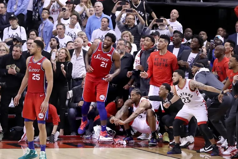 Sixers Ben Simmons (25) and Joel Embiid watching with everyone else as a shot by the Raptors' Kawhi Leonard (crouched down near corner) bounced four times on the rim before dropping in to end Game 7 of the NBA Eastern Conference semifinal series in Toronto on May 12.