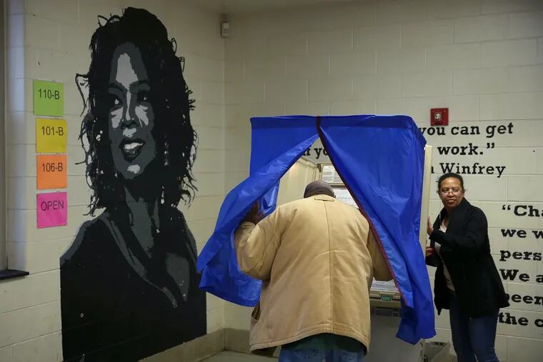 James Jones enters a voting booth as election judge Christy Carter, right, checks the machine next to a mural of Oprah Winfrey at Benjamin Franklin Elementary School, the Ward 35 Division 18 polling place, in Northeast Philadelphia on Tuesday, Nov. 6, 2018. Voters turned out despite at times heavy rain to participate in the midterm election.
